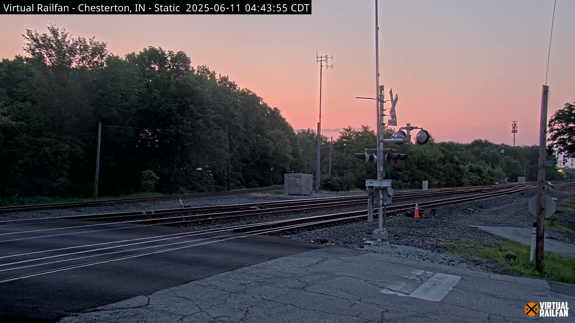 A railroad crossing with a traffic signal at dusk under a pinkish sky.