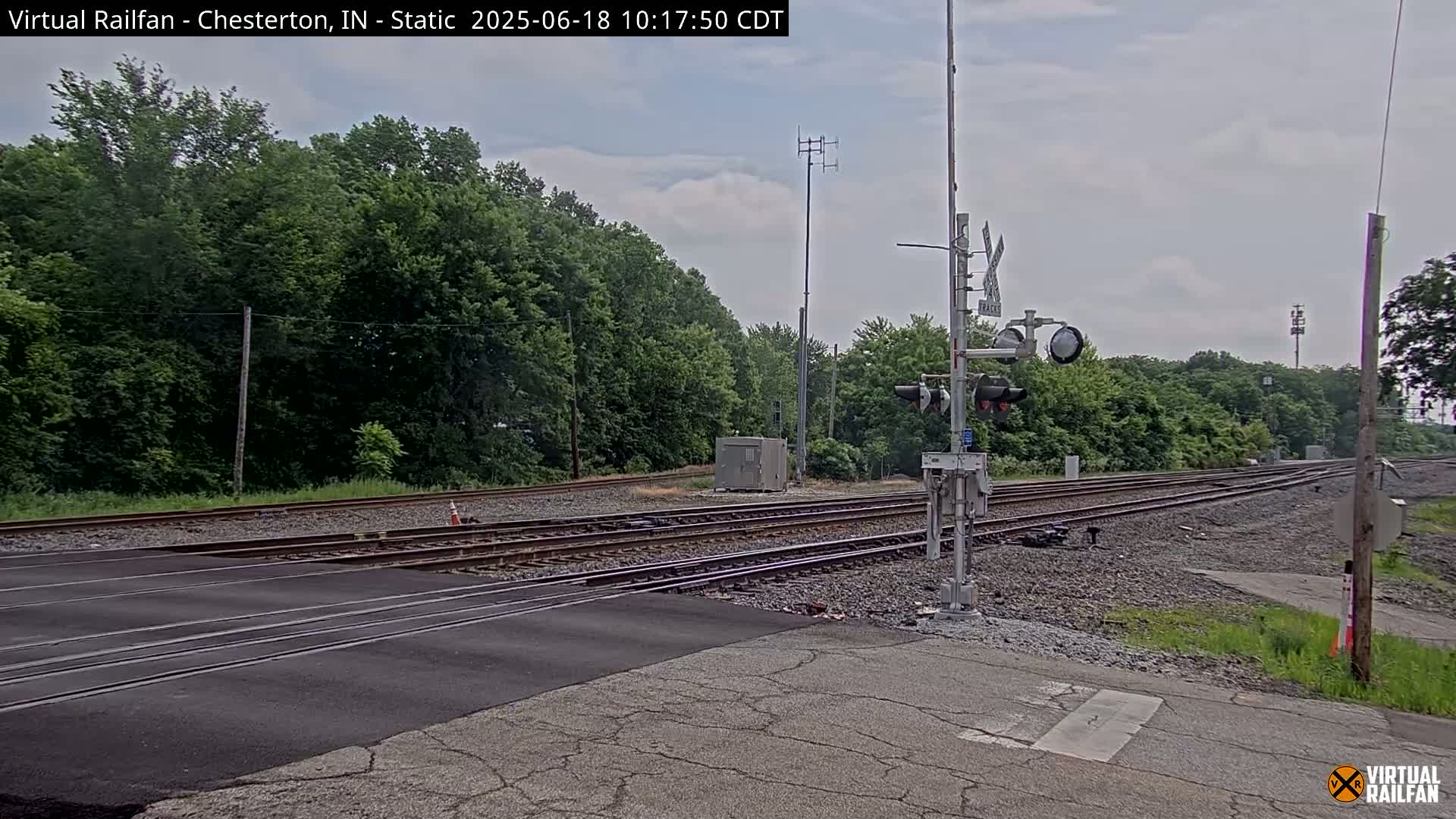 A railroad crossing with a roadway intersecting multiple train tracks under a partly cloudy sky.