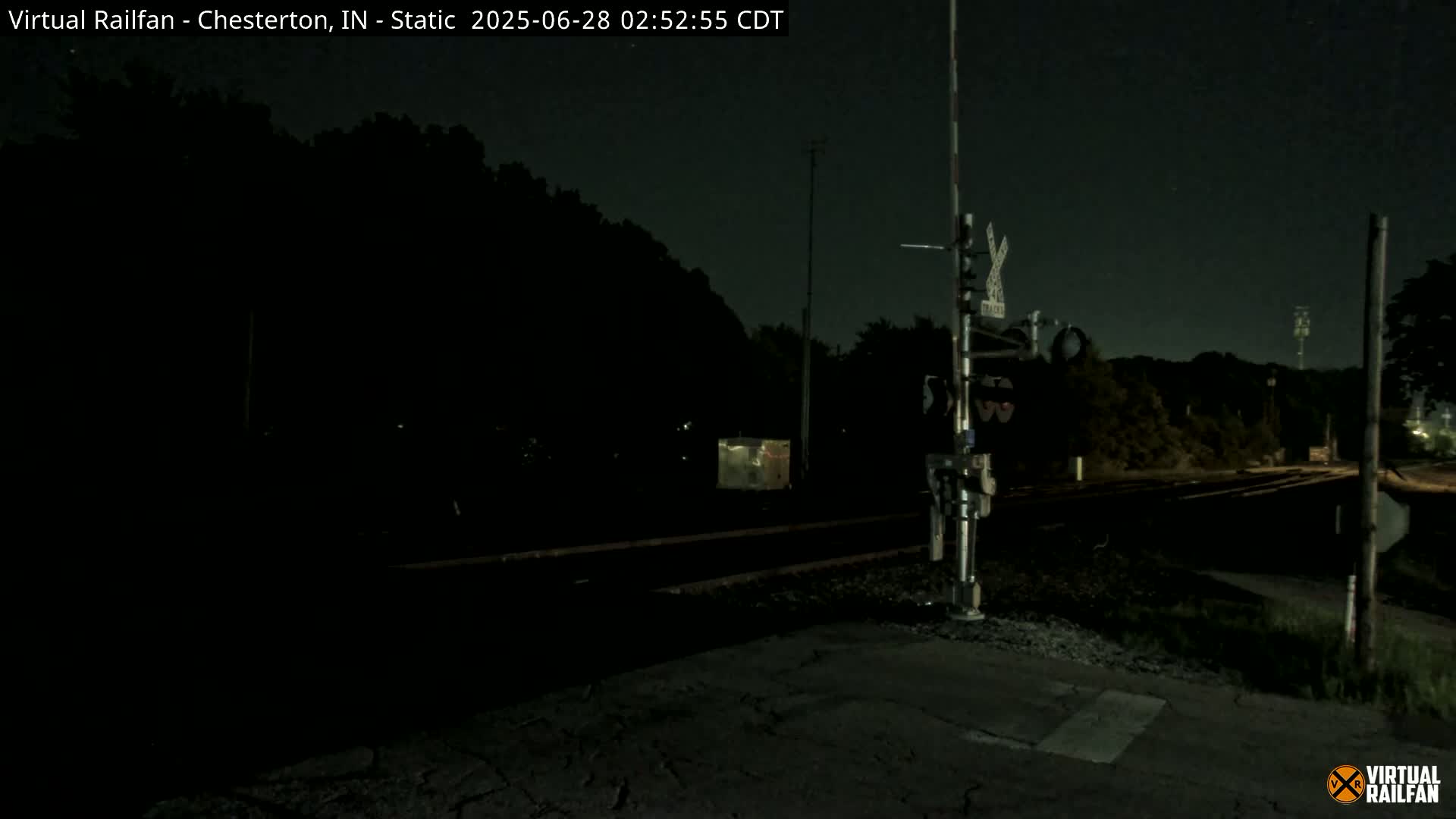 A nighttime view of a railroad crossing with a signal light, under a dark sky.