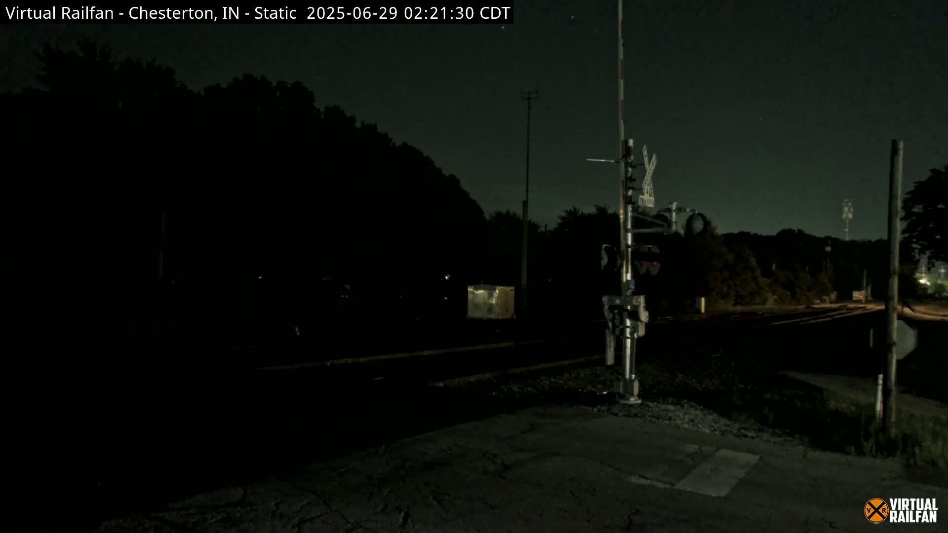 A nighttime view of a dark railroad crossing with a signal system under a clear, starry sky.
