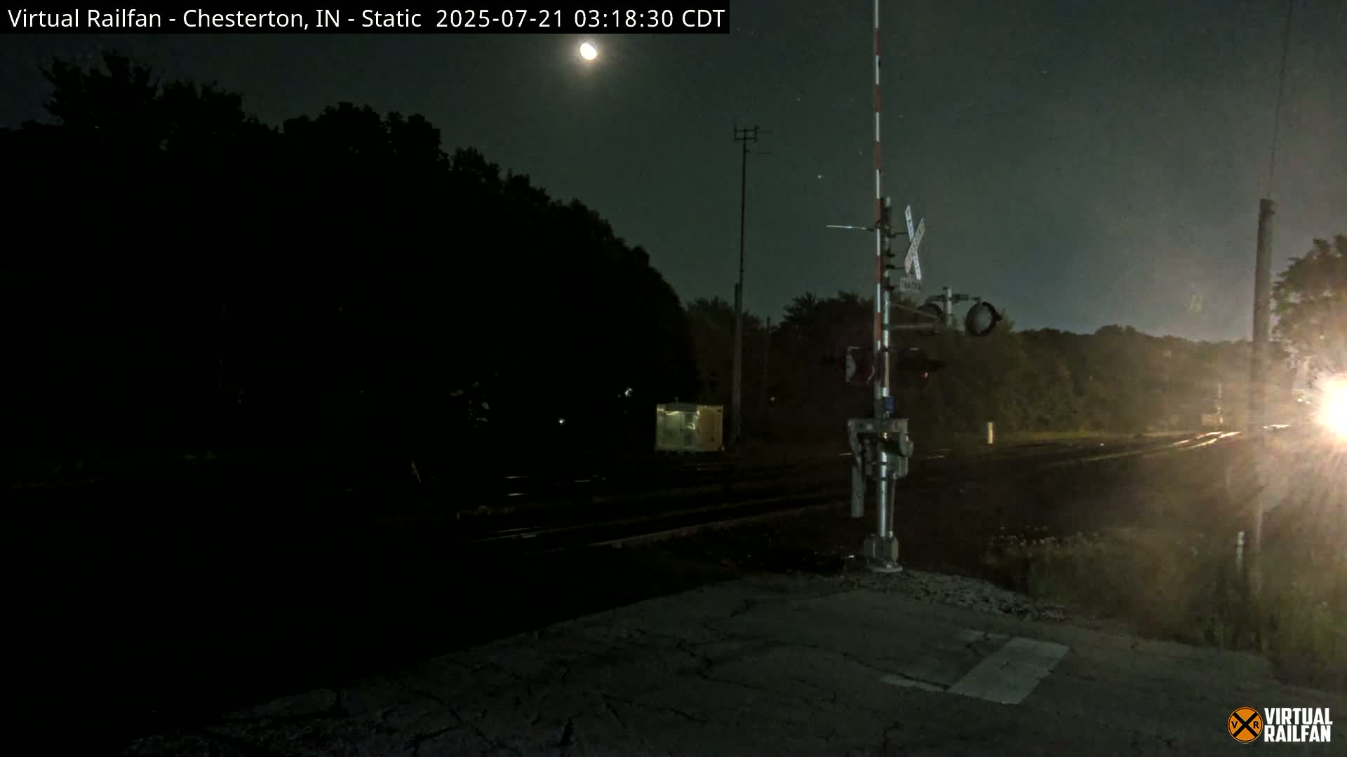 A nighttime view of a railroad crossing with a partially visible moon in a clear sky.
