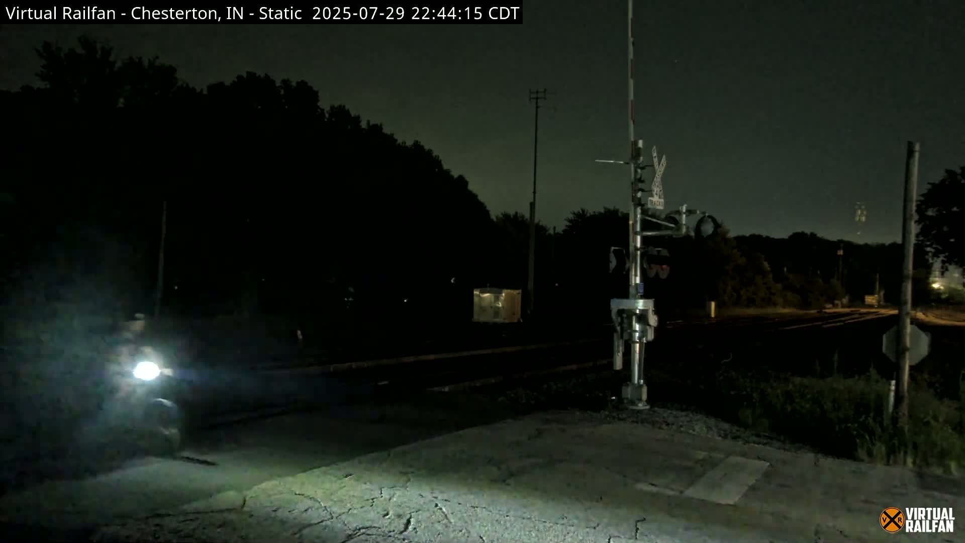 A nighttime view of a railroad crossing with a partially visible moon in a clear sky.