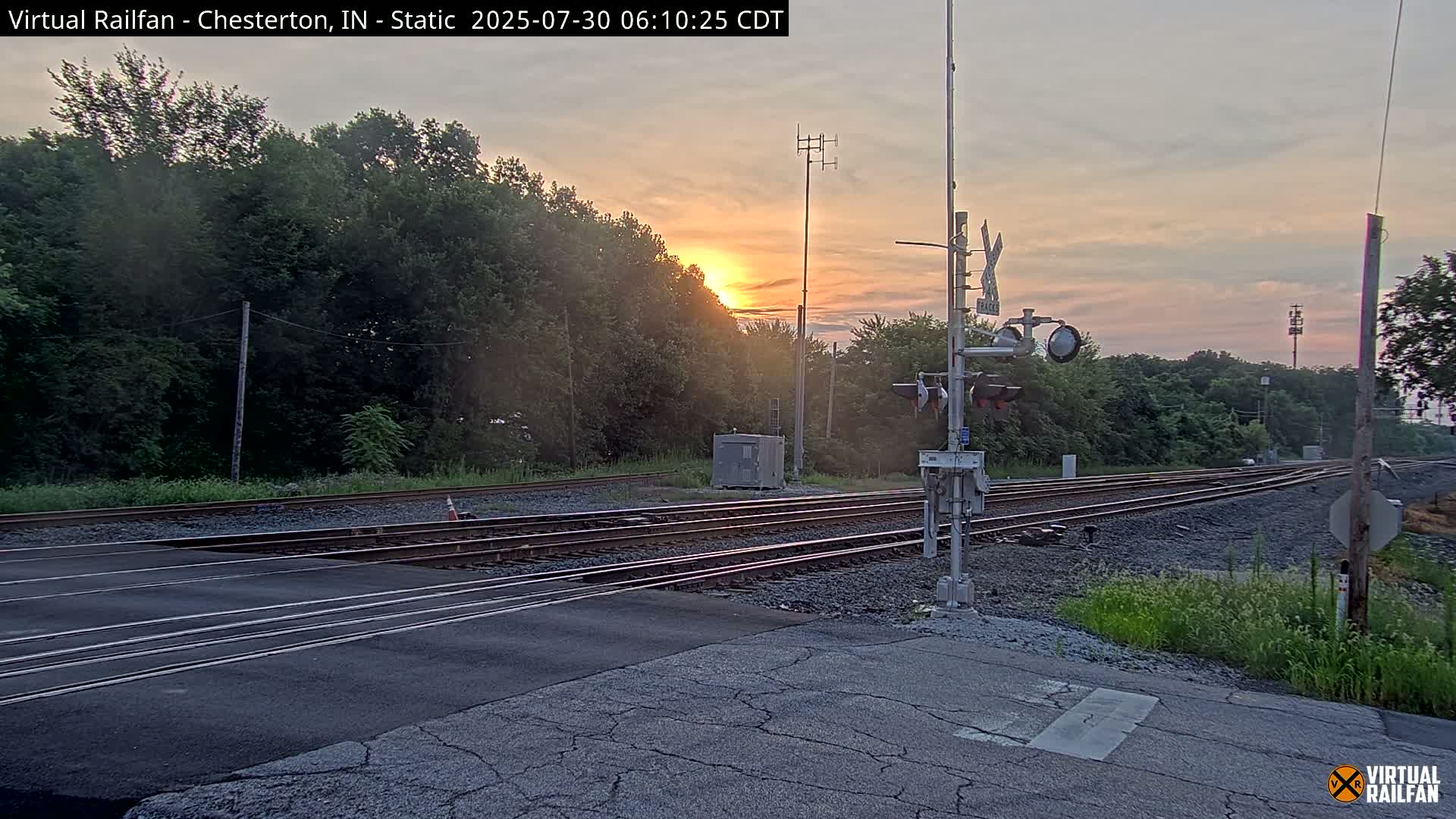 A nighttime view of a railroad crossing with a partially visible moon in a clear sky.