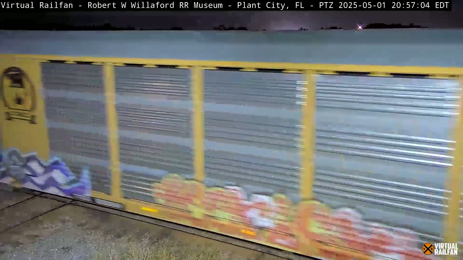 A graffiti-covered freight train car passes by at night under a dark sky.