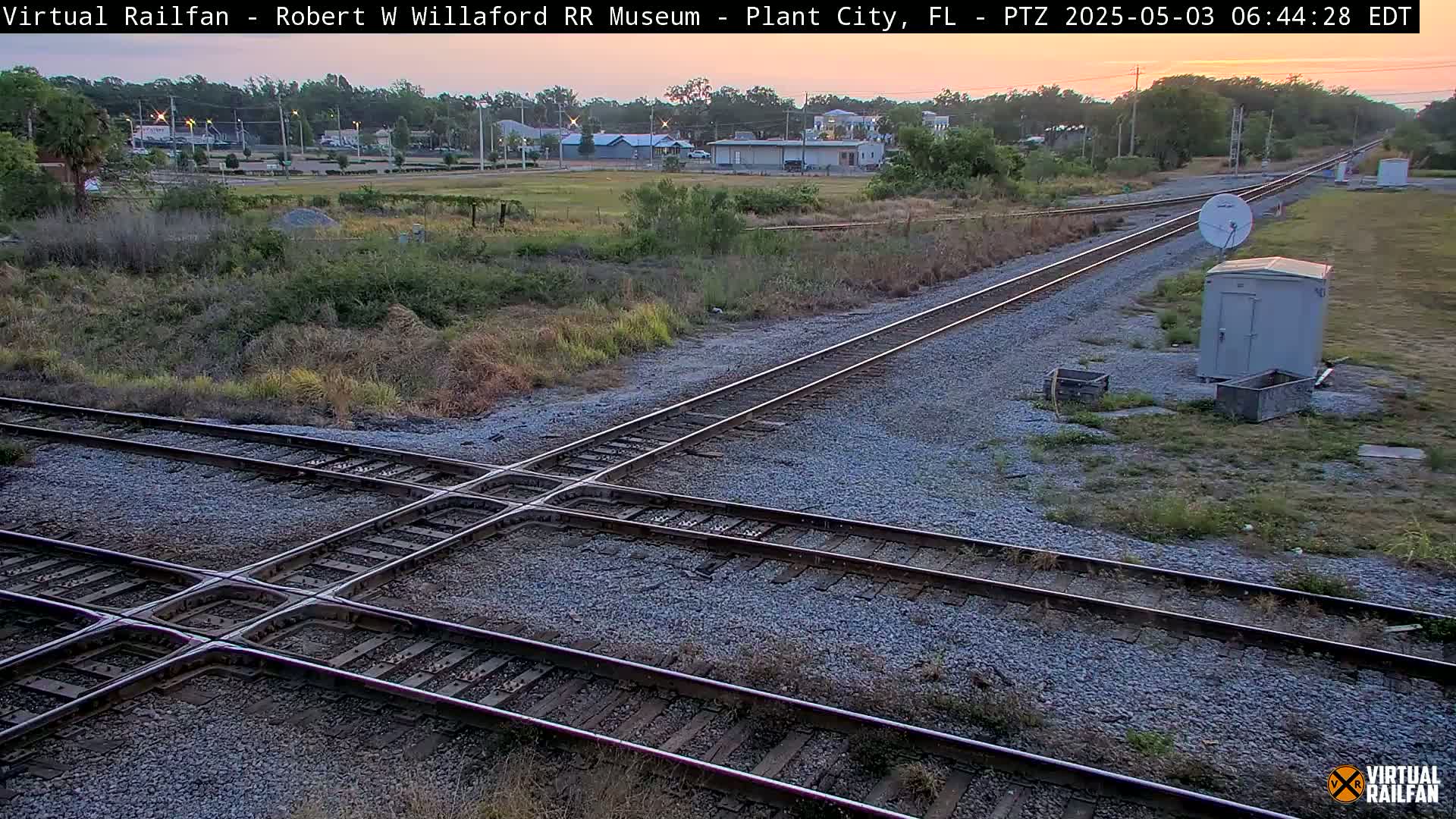 A railroad crossing with two sets of tracks intersects in a grassy area under a twilight sky.