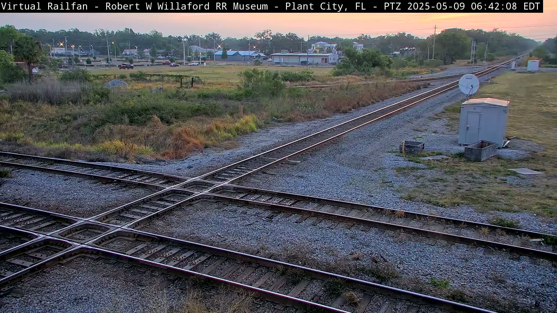 A train track intersection with a small building and satellite dish is visible under a twilight sky.