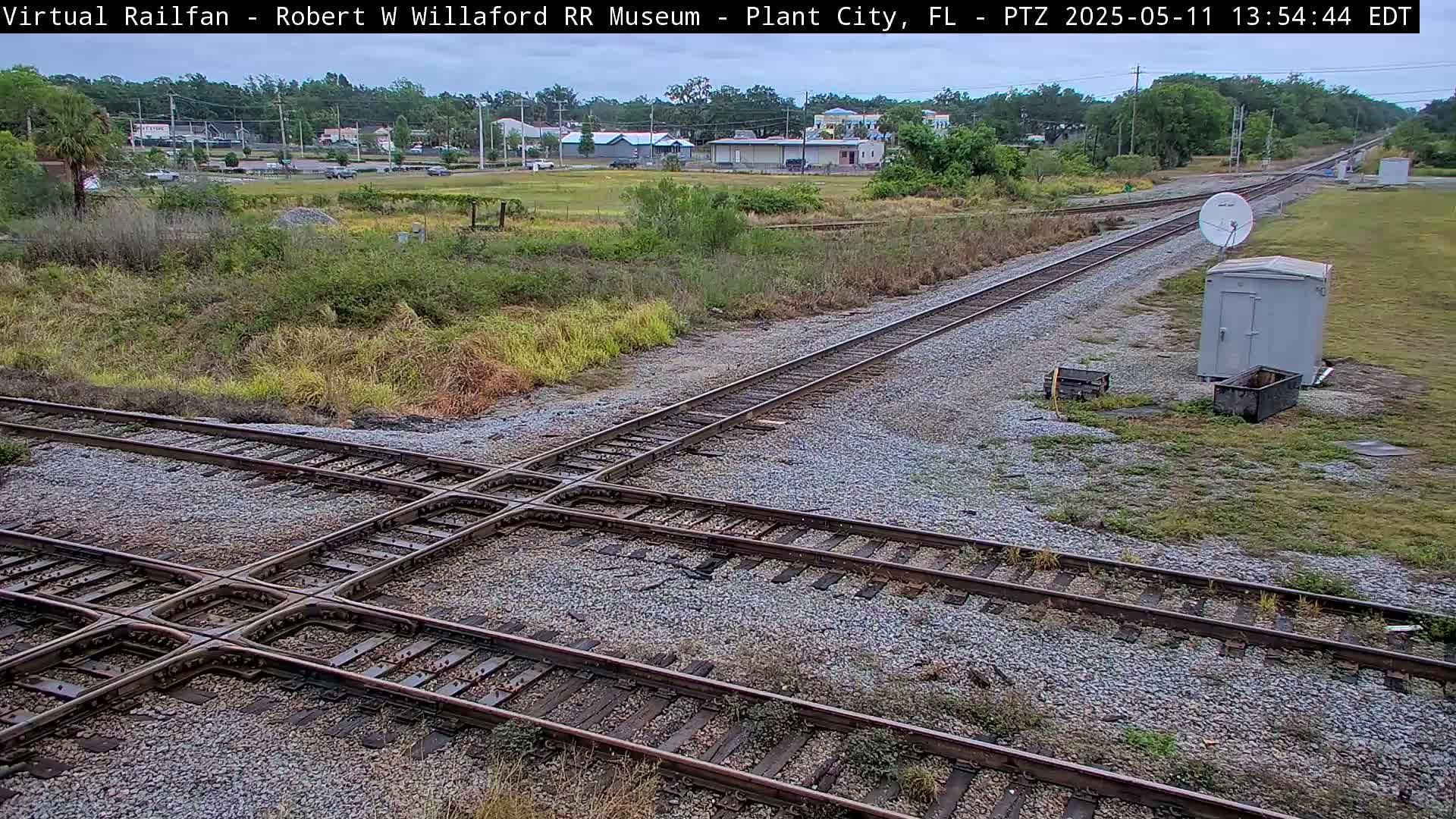A railroad crossing with several tracks is visible, and in the background is a small town under an overcast sky.