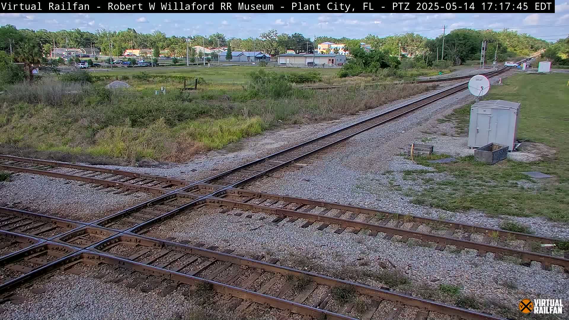A high-angle view of a railroad crossing with two sets of tracks intersecting, under a mostly clear sky.