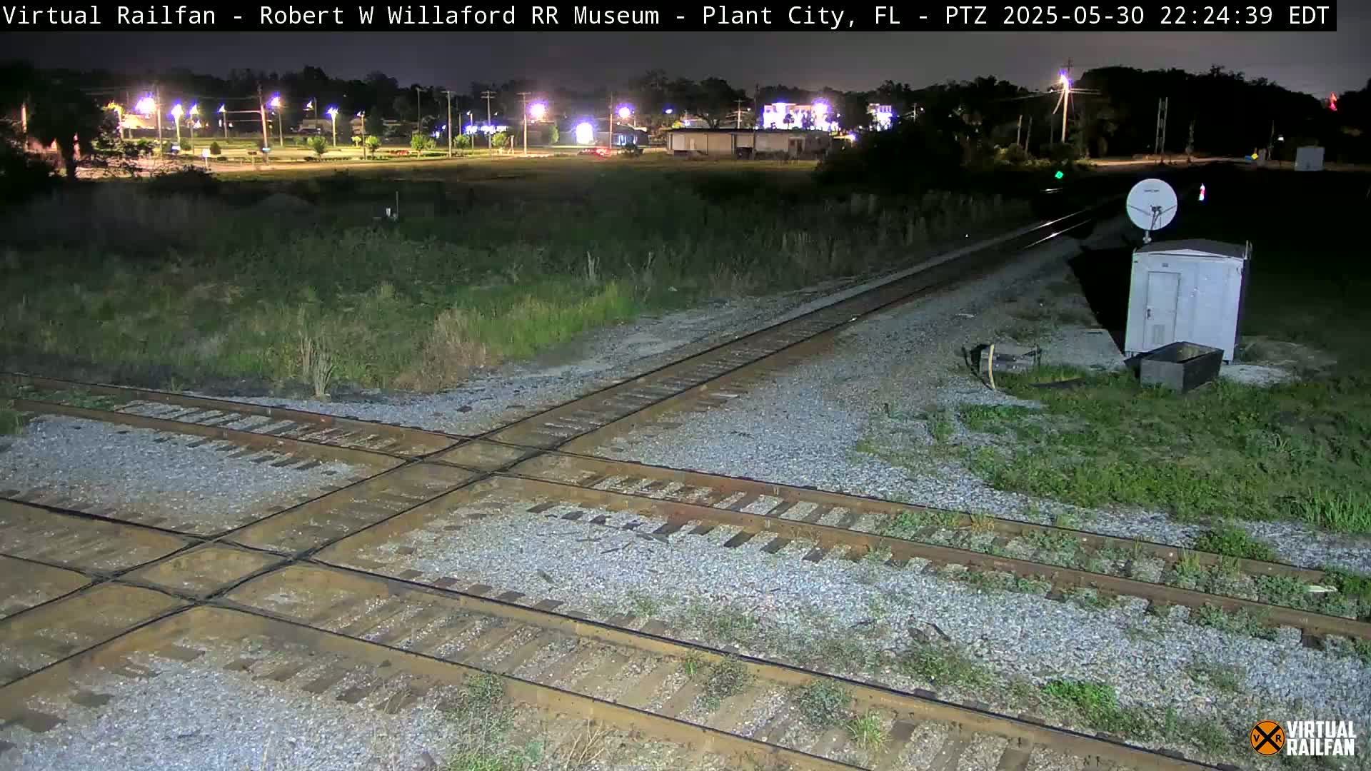 A nighttime view of a railroad crossing with intersecting tracks, surrounded by sparse vegetation under a clear sky.