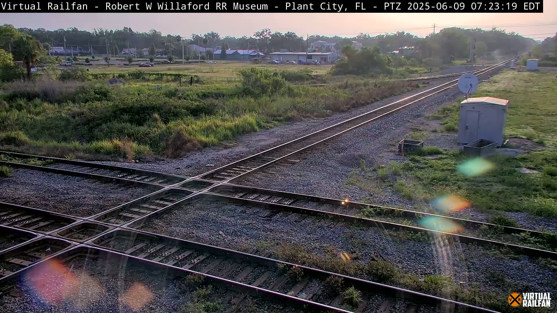 A high-angle view of a railway crossing in a grassy area under a partly sunny sky.