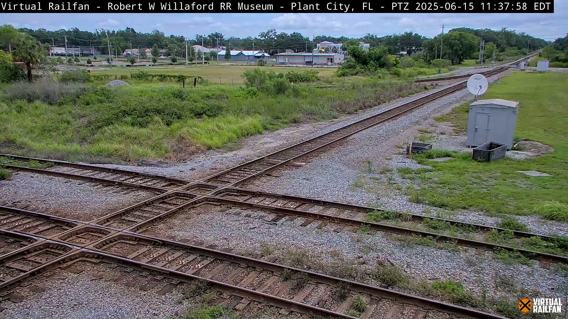 A railroad crossing with train tracks intersecting, situated in a grassy area under a partly cloudy sky.