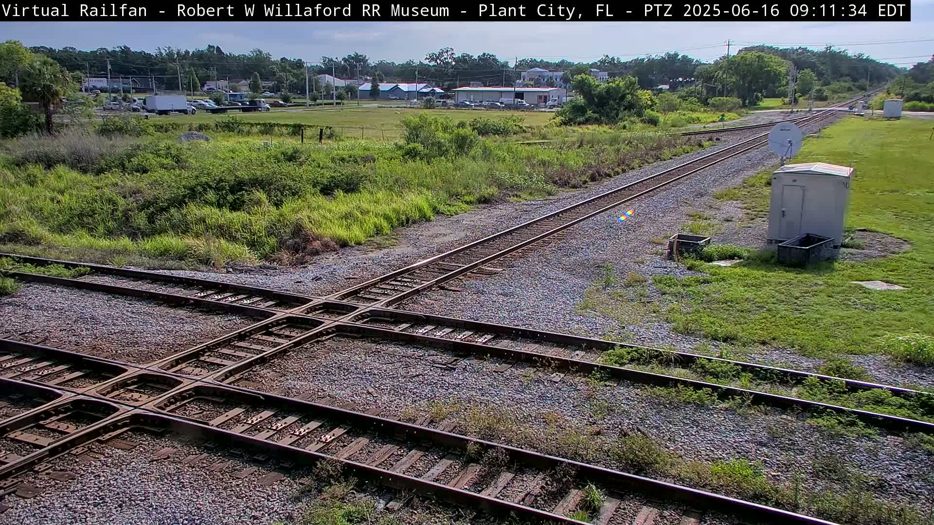 A high-angle view of a railroad crossing in a grassy area under a partly sunny sky.