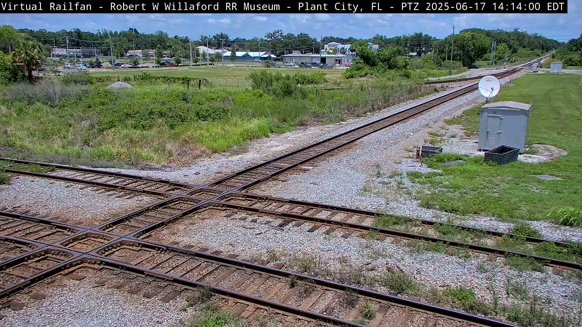 A train track intersection with a satellite dish and small building is visible in a sunny, outdoor setting.