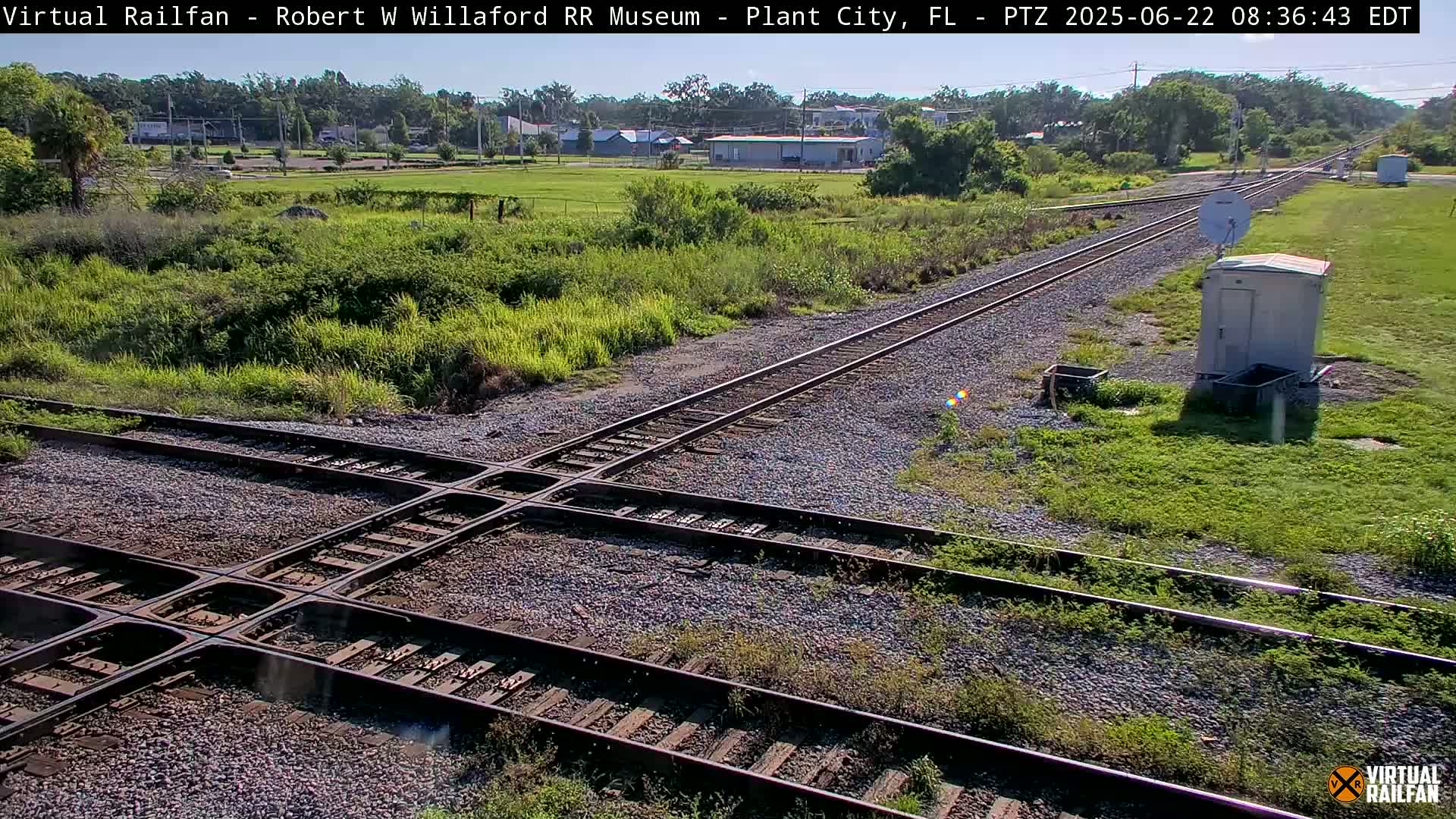 A high-angle view of a railroad crossing with two sets of tracks intersecting in a sunny, outdoor setting.