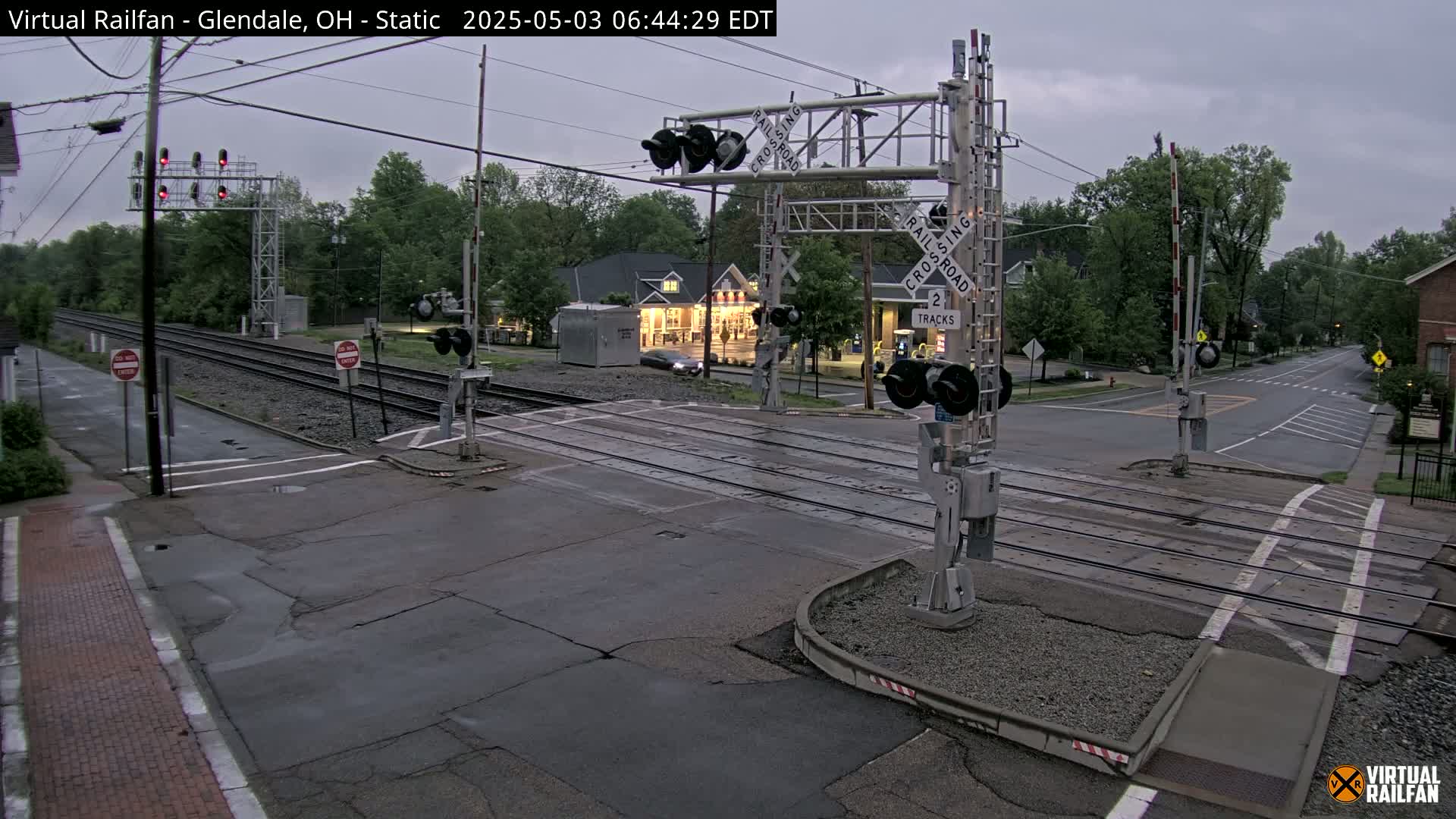 A railroad crossing with lowered gates under an overcast sky shows a street intersecting the tracks.