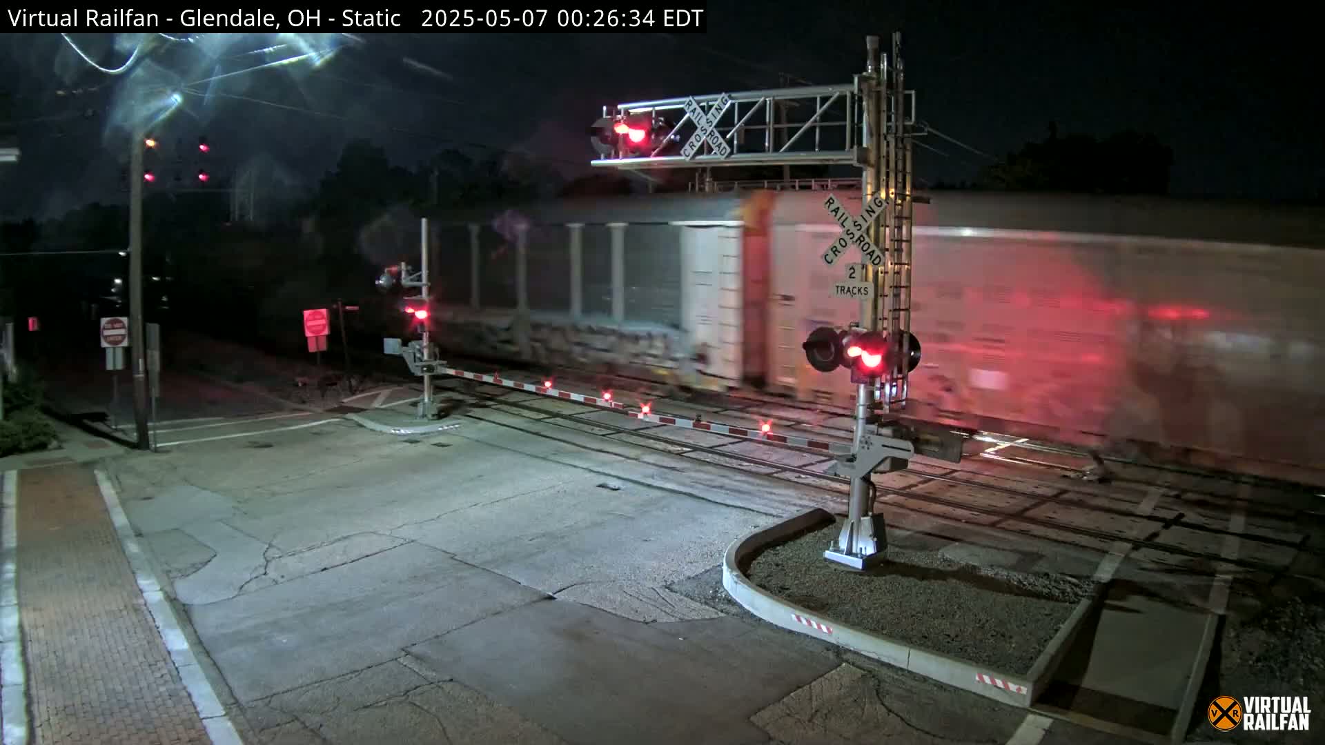 A long freight train passes through a railroad crossing at night.