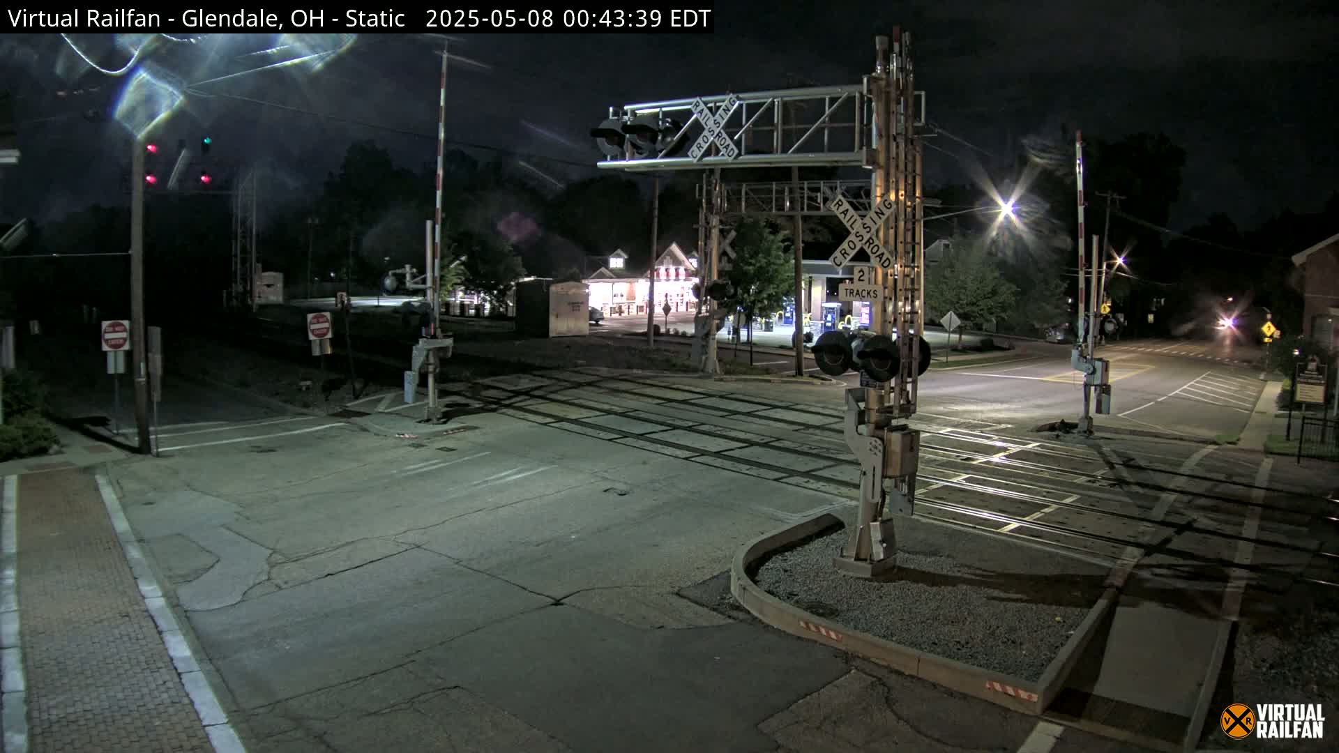 A nighttime view of a deserted railroad crossing with raised gates and flashing lights.