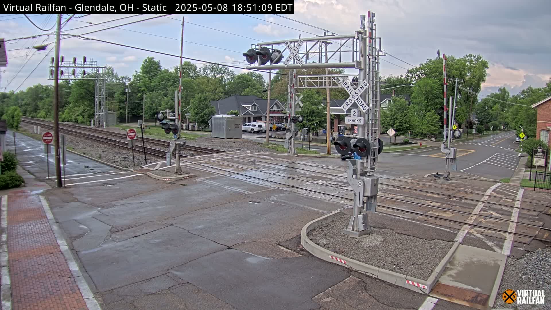 A railroad crossing with lowered gates is shown under an overcast sky;  a street intersects the tracks.