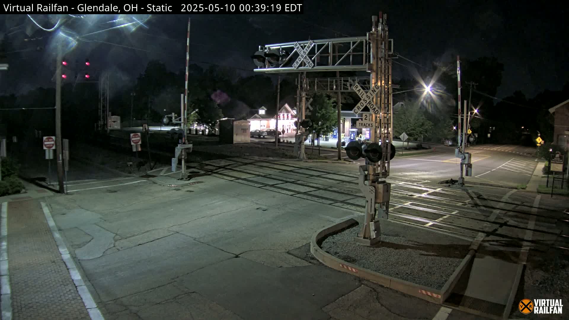 A nighttime view of a railroad crossing with its gates down, illuminated by streetlights, under a clear, dark sky.
