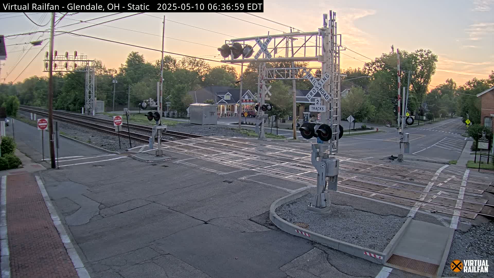 A railroad crossing with two tracks is shown at sunrise, under a mostly clear sky.