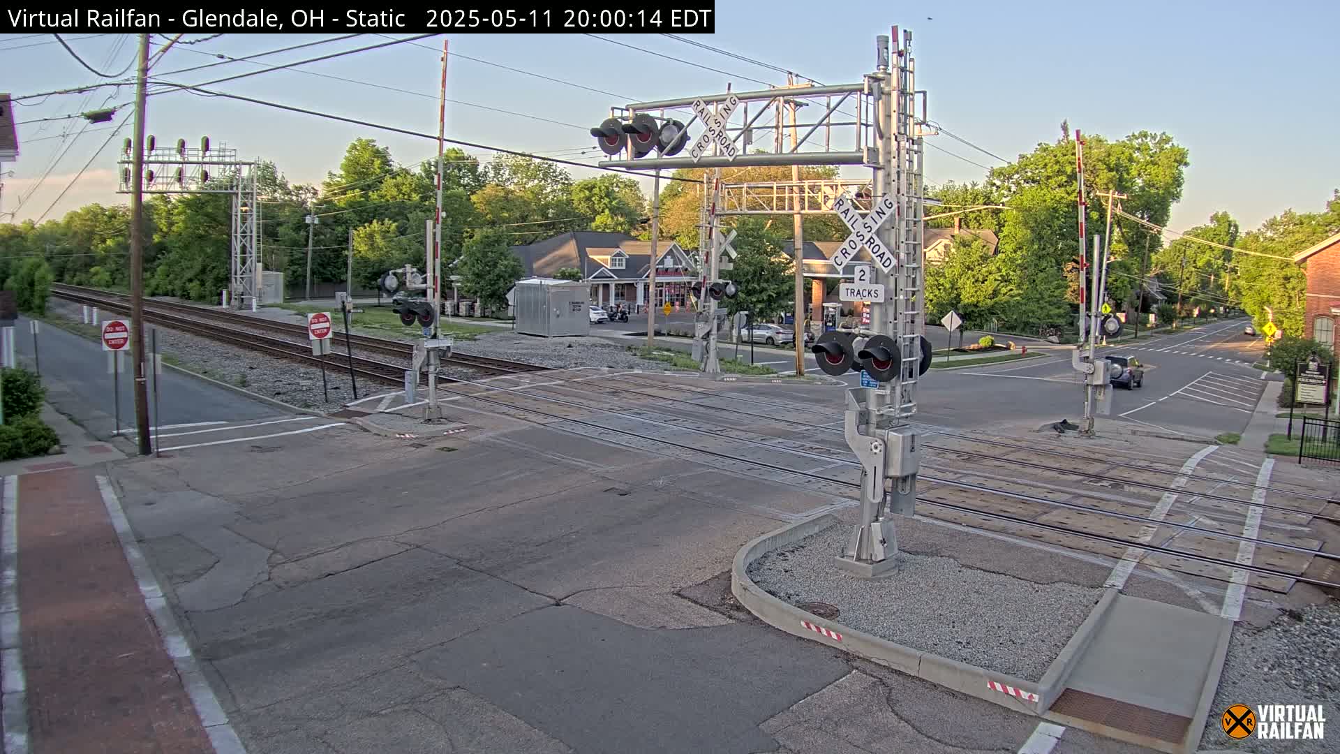 A railroad crossing with lowered gates is shown at dusk, under a clear sky.