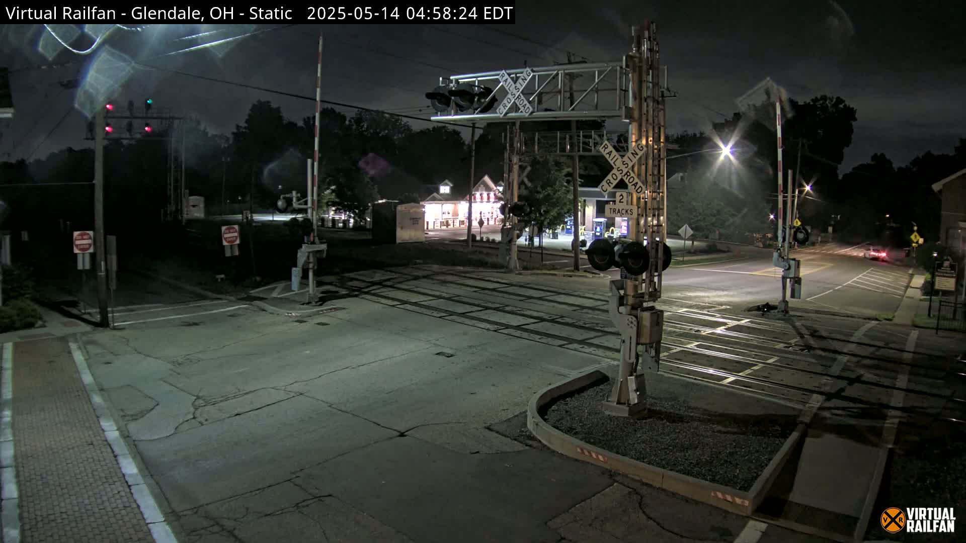 A nighttime view of a quiet railroad crossing with lowered gates, illuminated by streetlights.
