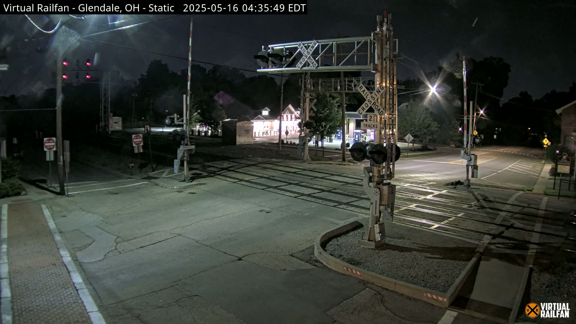 A nighttime view of a railroad crossing with its gates down, illuminated by streetlights and the crossing signals.