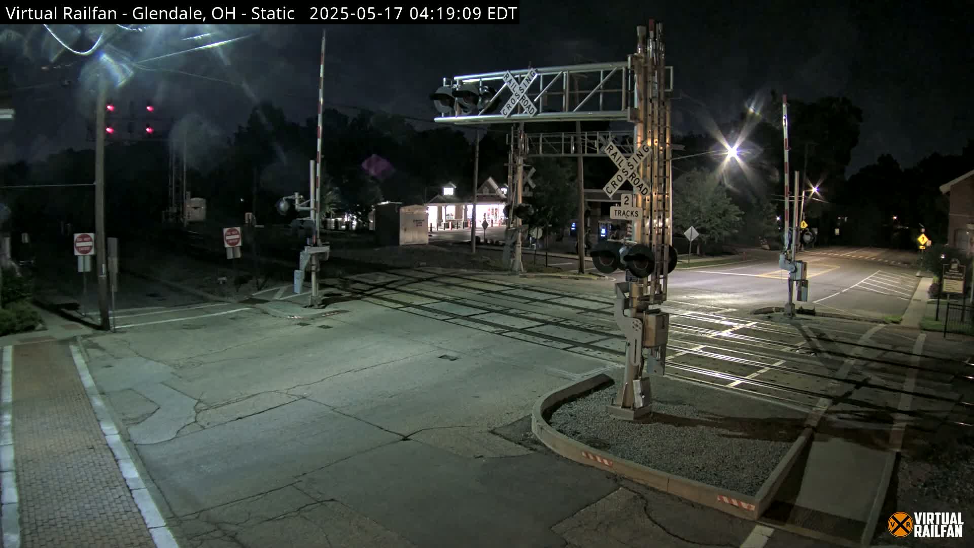 A nighttime view of a two-track railroad crossing with crossing gates down and red lights illuminated.