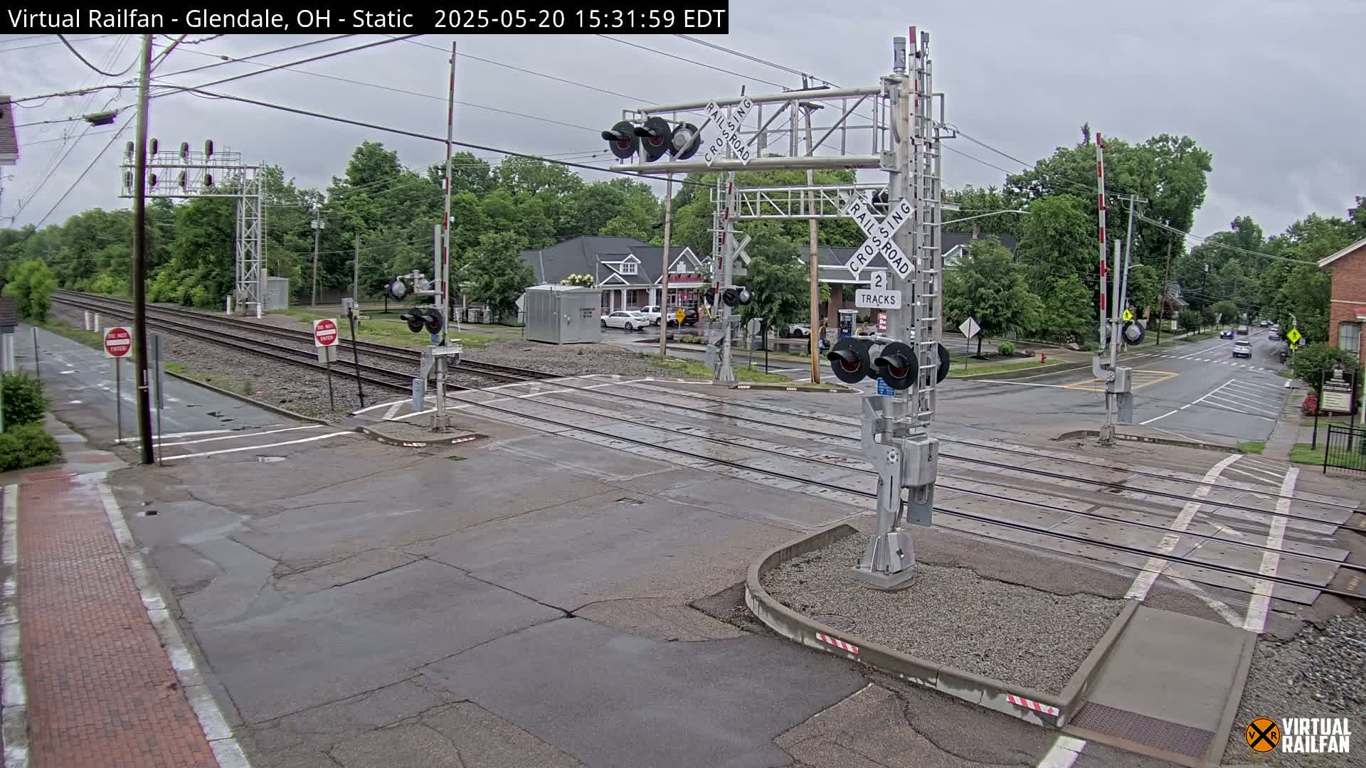 A railroad crossing with lowered gates is shown under an overcast sky, with a street intersecting the tracks.