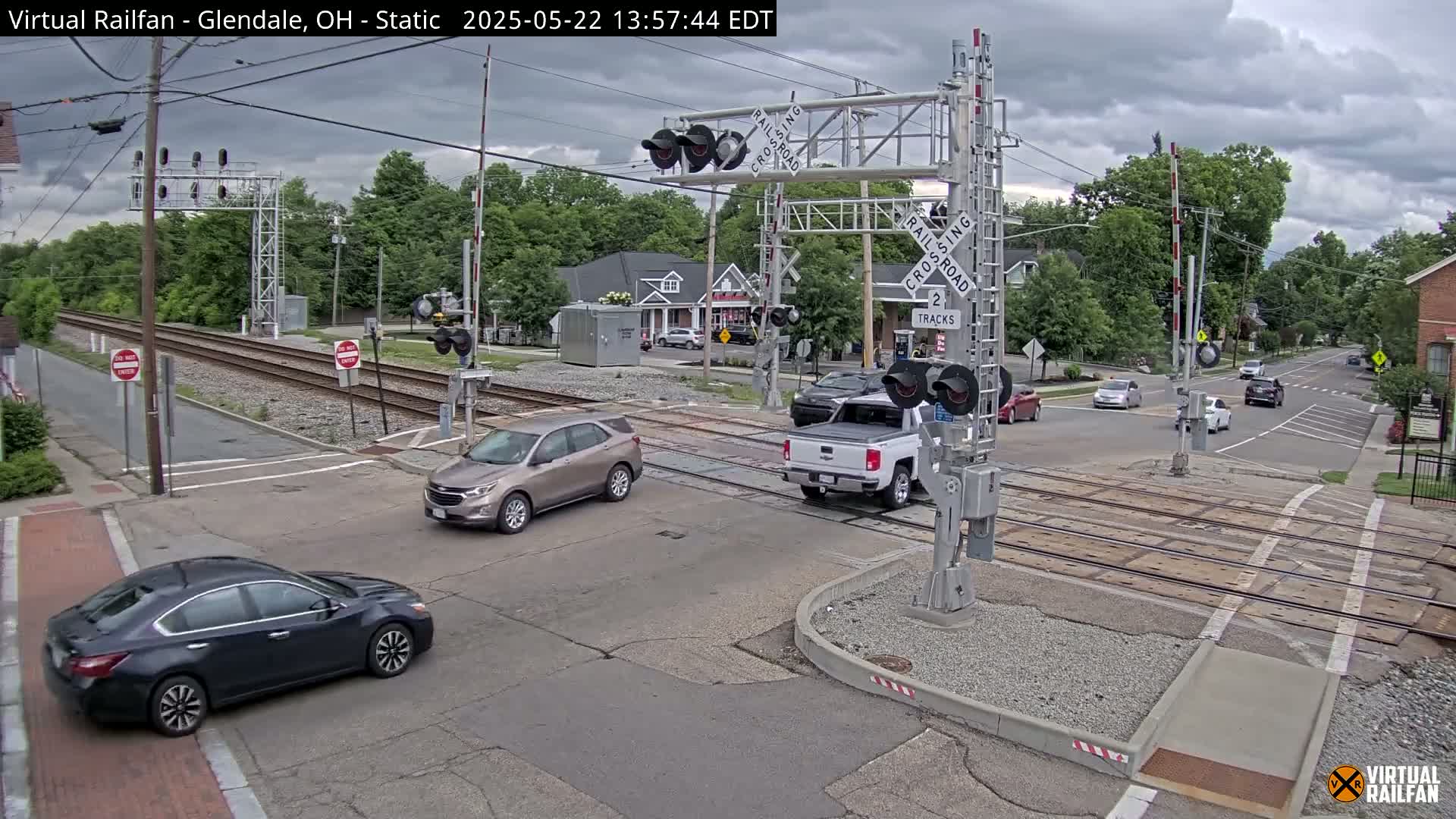 A railroad crossing with several cars stopped at the intersection under a cloudy sky.