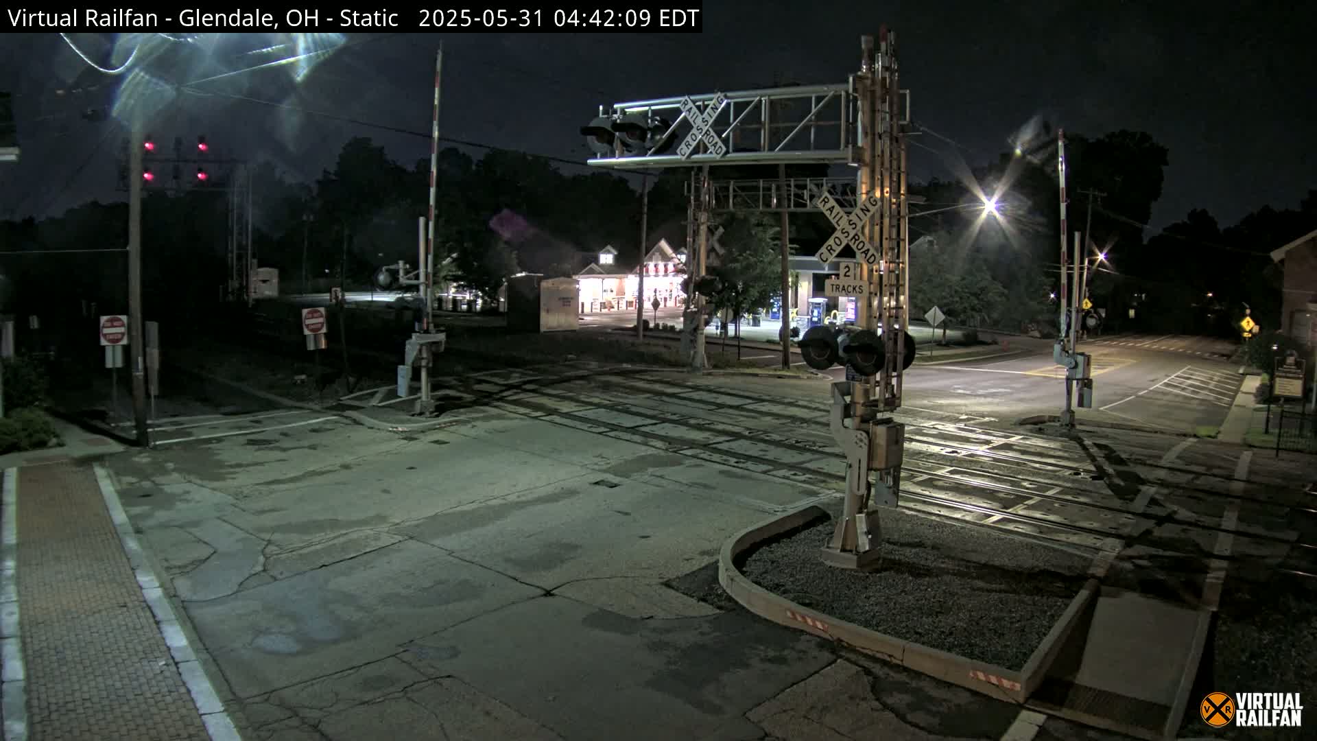 A nighttime view of a railroad crossing with its gates down, illuminated by streetlights, under a clear sky.