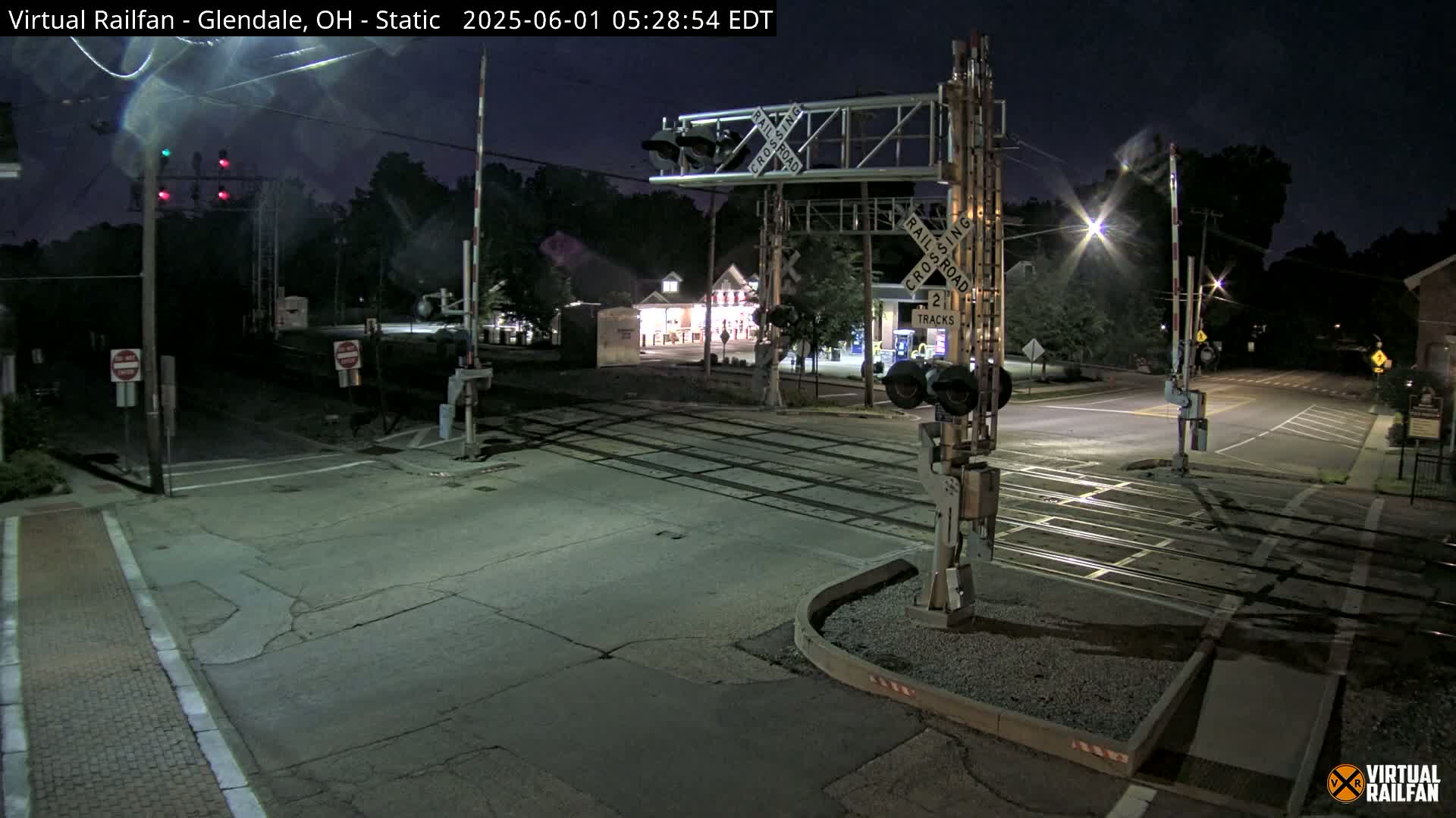 A nighttime view of a railroad crossing with traffic lights and crossing gates, under a dark sky.