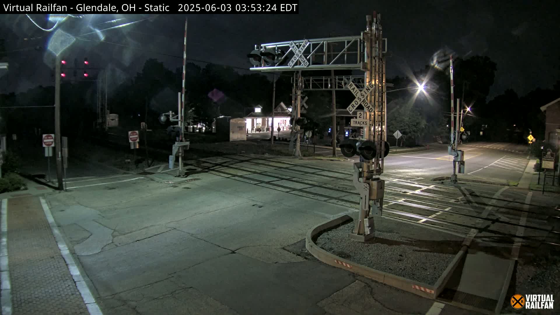 A nighttime view of a railroad crossing with lowered gates and flashing lights, showing an empty intersection.