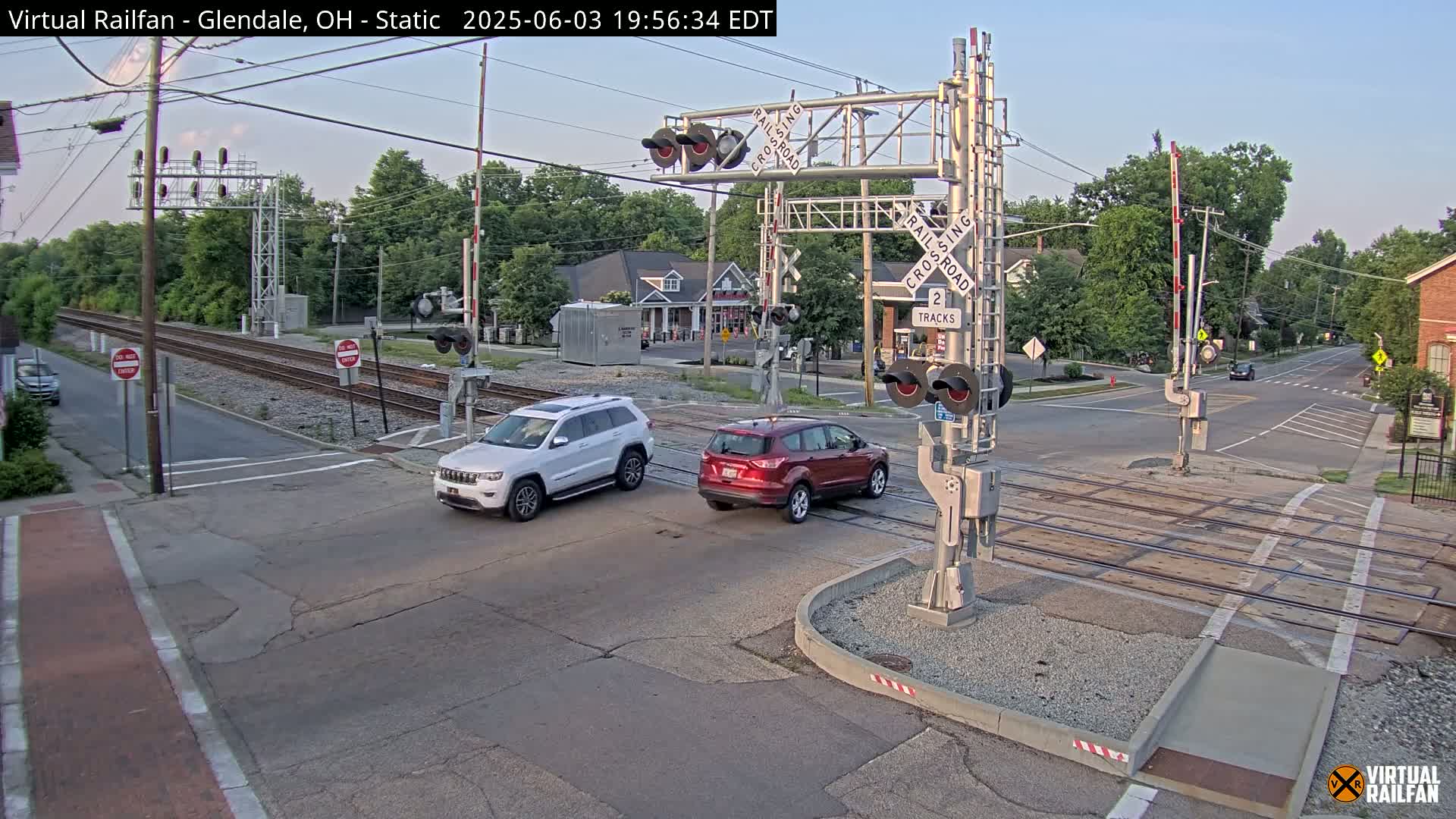 Two SUVs are stopped at a railroad crossing under a clear evening sky.