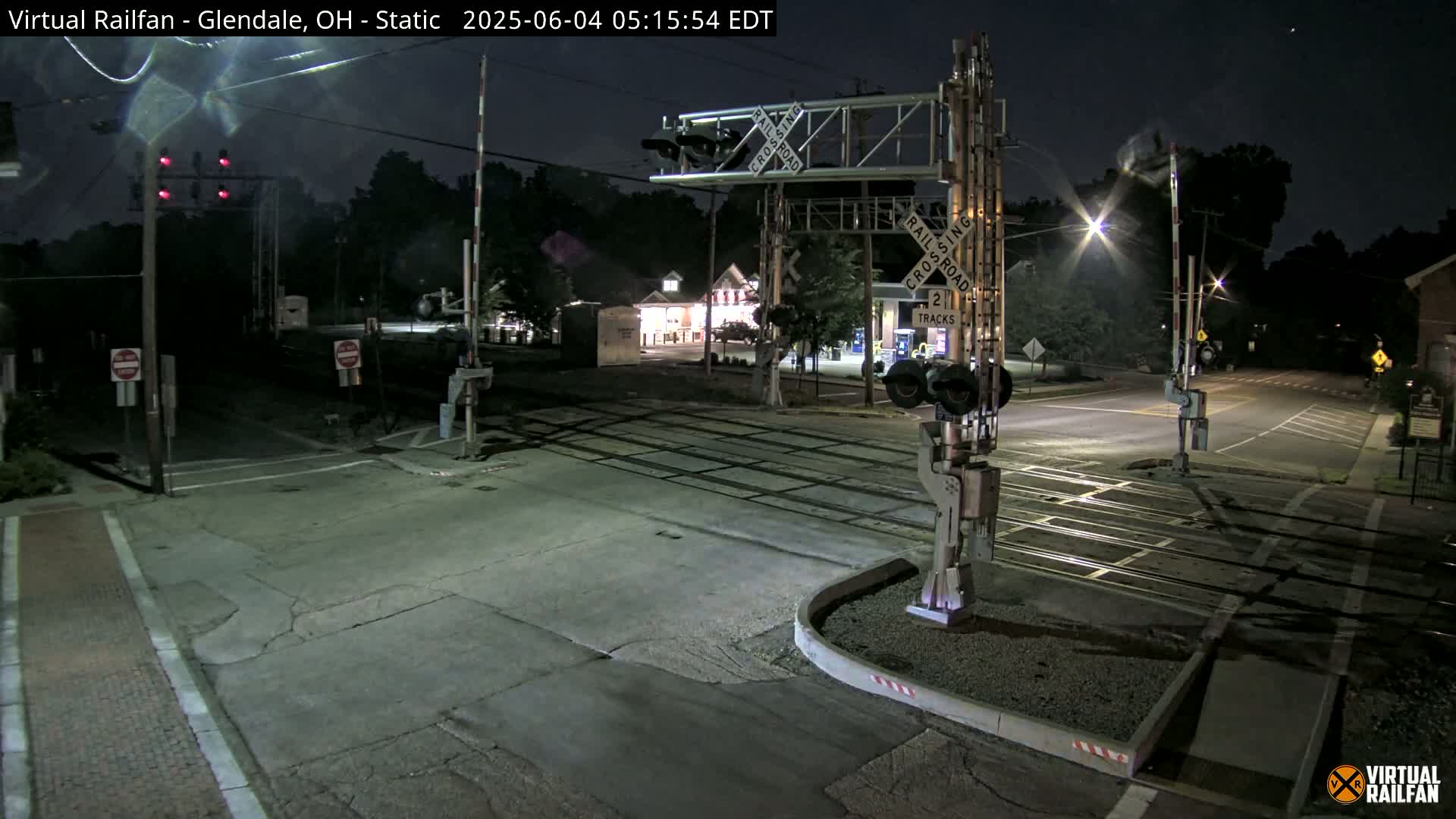 A nighttime view of a railroad crossing with traffic lights and crossing gates down, illuminated by streetlights.
