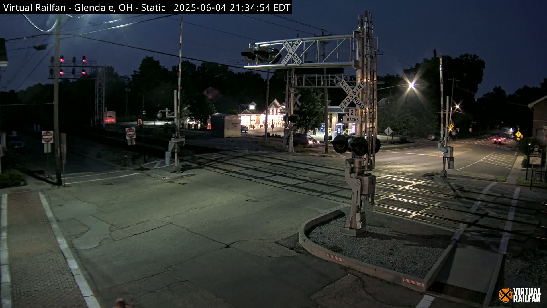 A nighttime view of a railroad crossing with its gates down, illuminated by streetlights, under a dark sky.