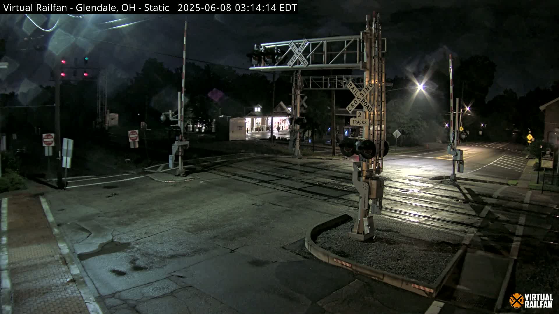 A nighttime view of a wet railroad crossing with its gates down and lights flashing.