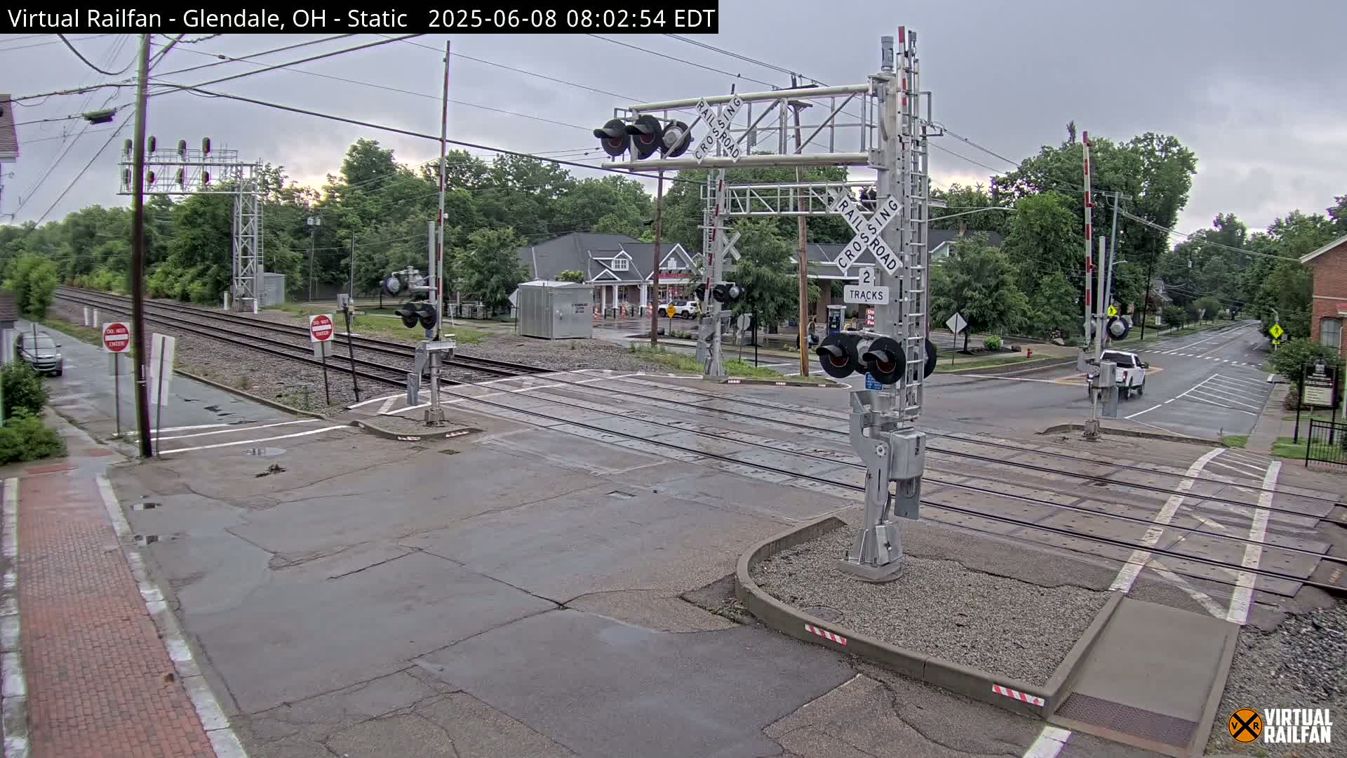 A railroad crossing with lowered gates under an overcast sky, showing a street intersecting with two train tracks.