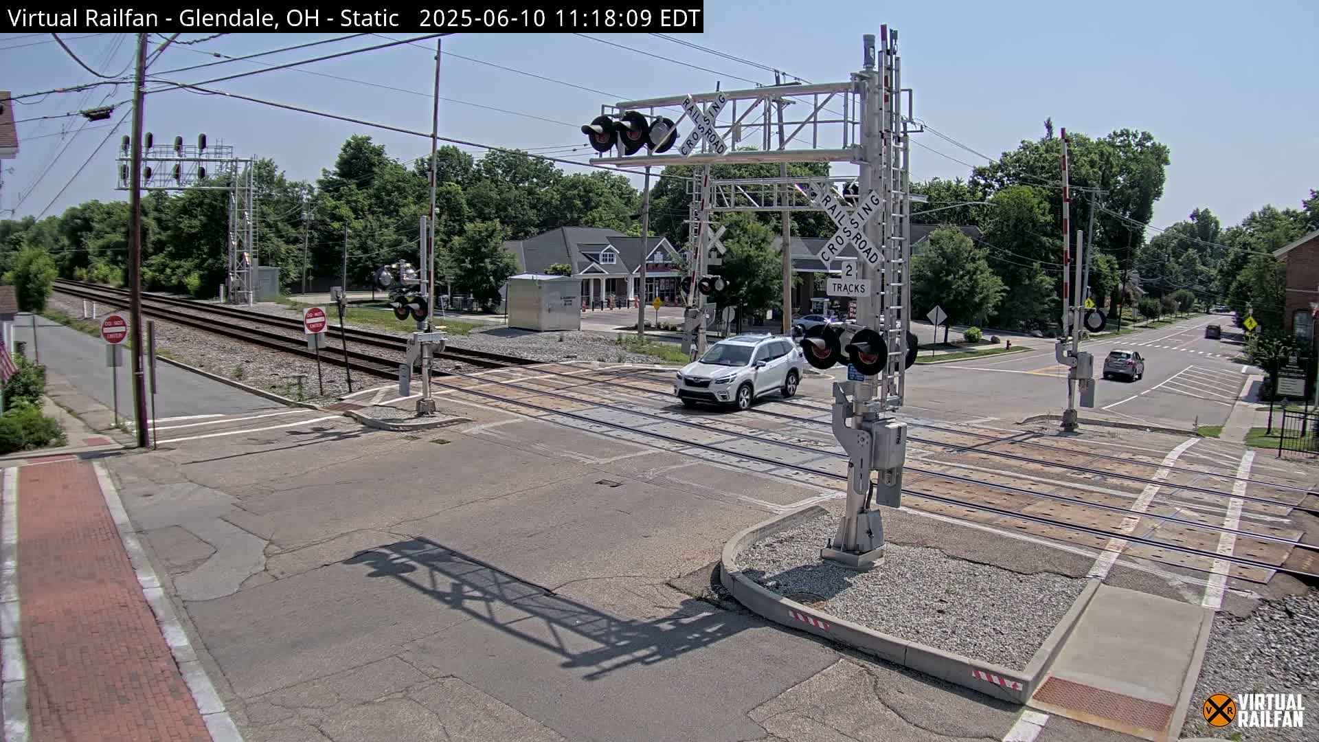 A white SUV crosses a railroad track at a road intersection under a sunny sky.