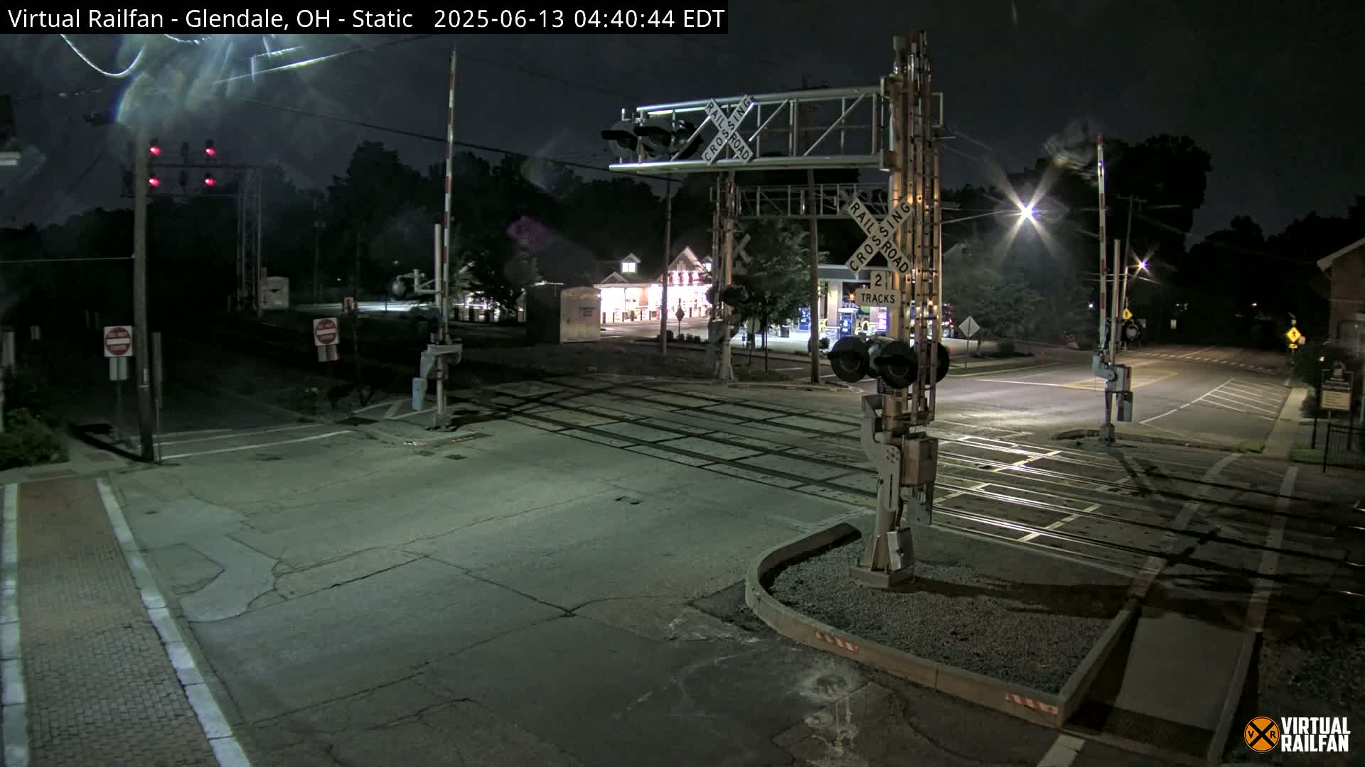 A nighttime view of a railroad crossing with traffic lights and gates, illuminated by streetlights under a clear sky.