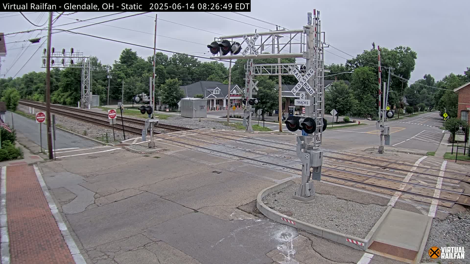 A railroad crossing with lowered gates is shown on an overcast day; the road and surrounding area are mostly empty.