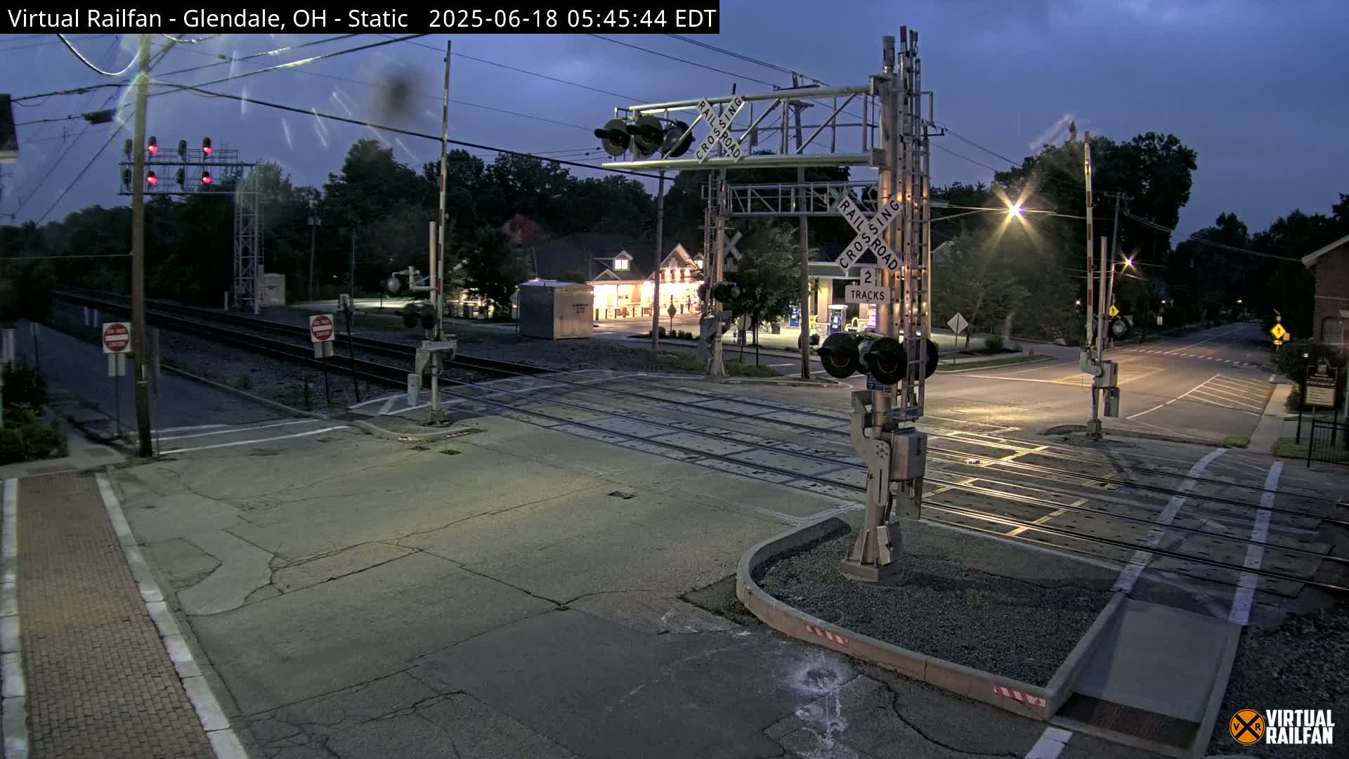 A nighttime view of a railroad crossing with lowered gates and flashing lights under a twilight sky.