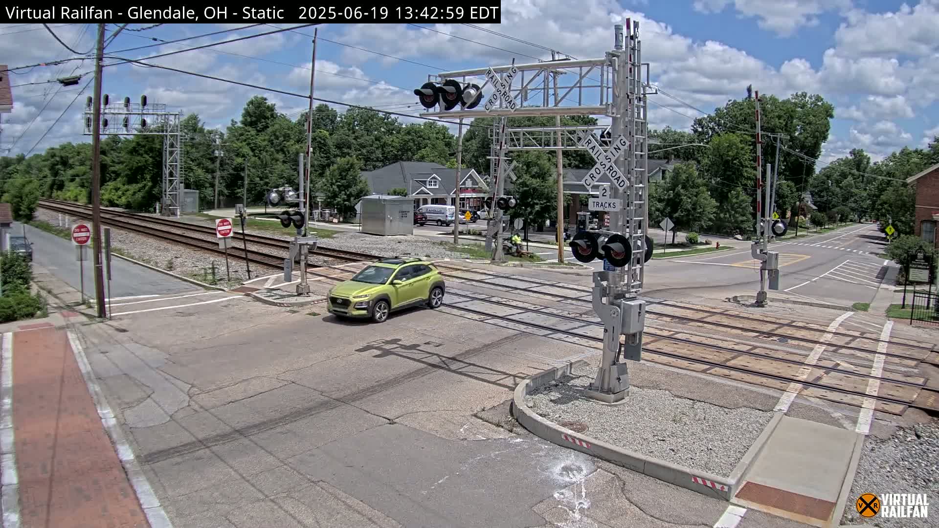 A lime-green SUV drives across a railroad crossing under a partly cloudy sky.