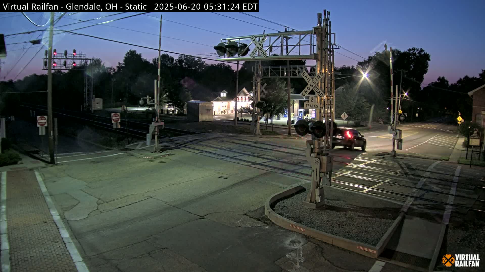 A nighttime view of a railroad crossing with a single vehicle passing through, under a twilight sky.