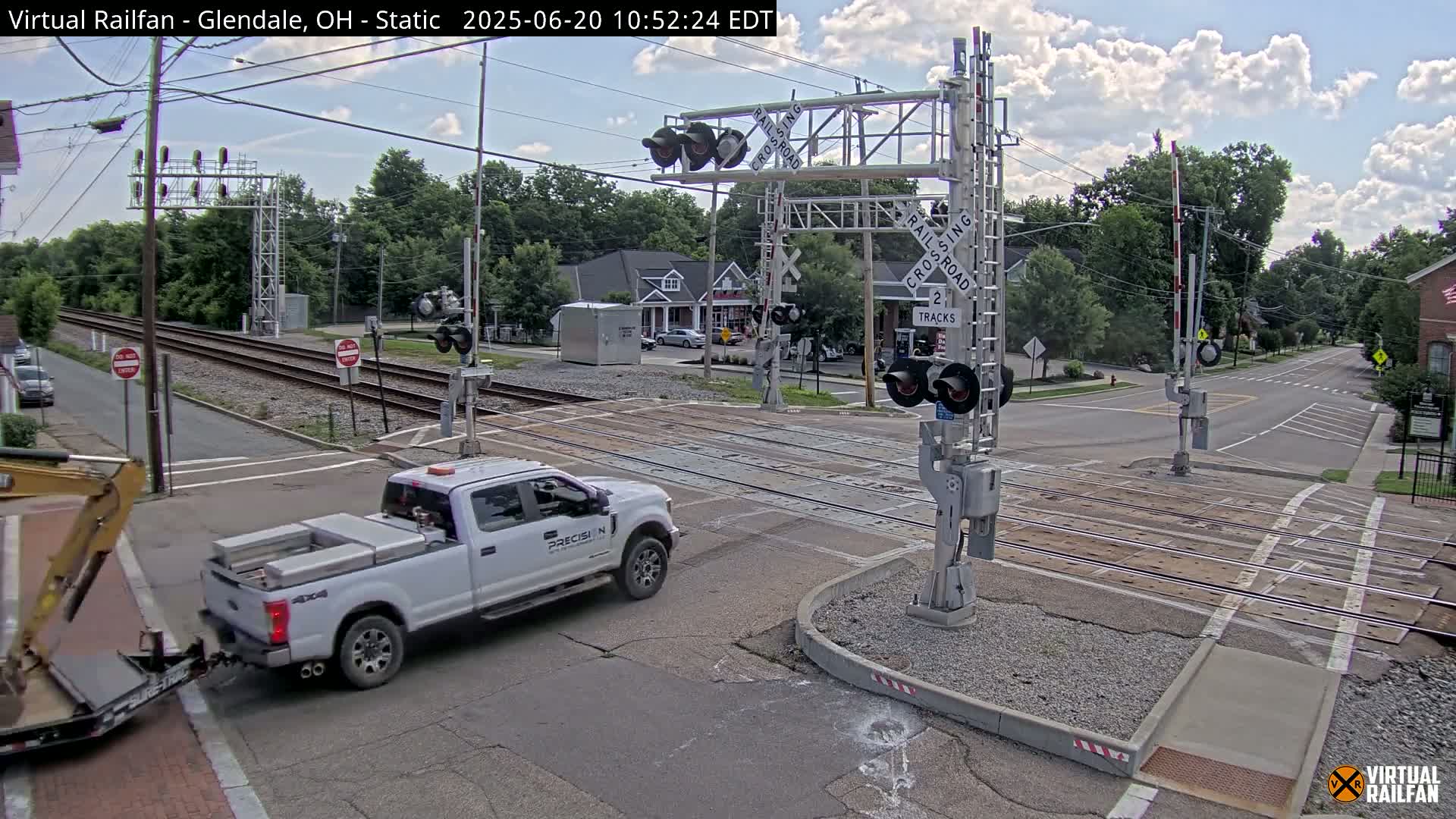 A white pickup truck towing a small trailer is driving across a railroad crossing under a partly cloudy sky.