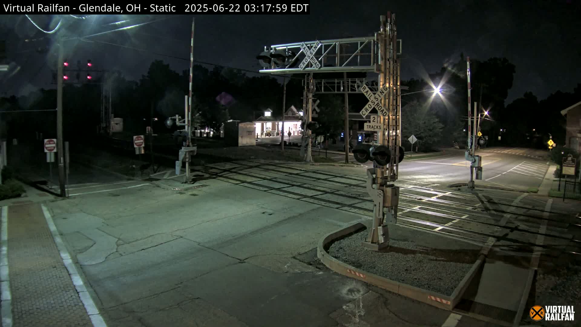 A nighttime view of a railroad crossing with lowered gates and red signal lights, under clear skies.