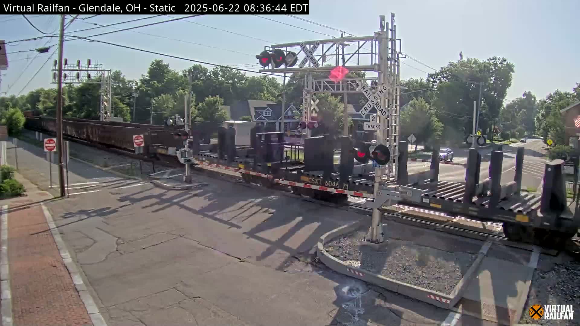 A long freight train passes through a railroad crossing on a sunny day.