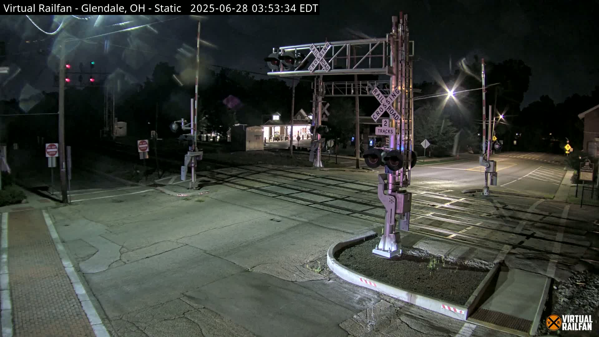 A nighttime view of a deserted railroad crossing with raised gates and flashing lights.