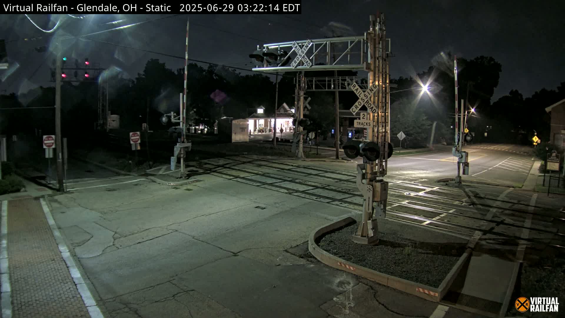 A nighttime view of a deserted railroad crossing with lowered gates and illuminated crossing signals.