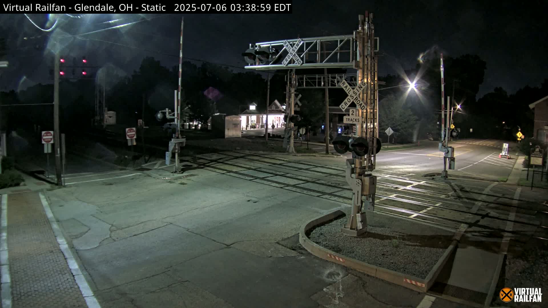 A nighttime view of a deserted two-track railroad crossing with lowered gates and red signal lights.